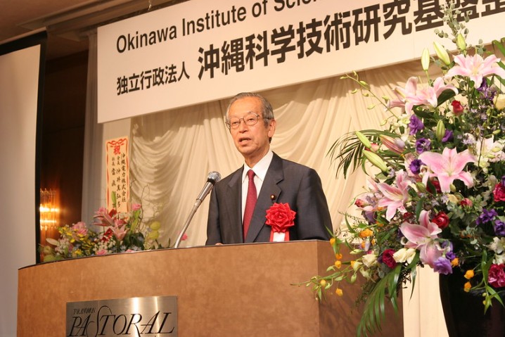 Koji Omi speaking in front of  a podium