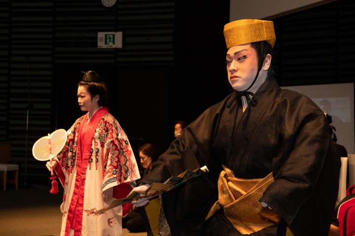Female and male dancers dressed in traditional Ryukyuan costume dance with fans.