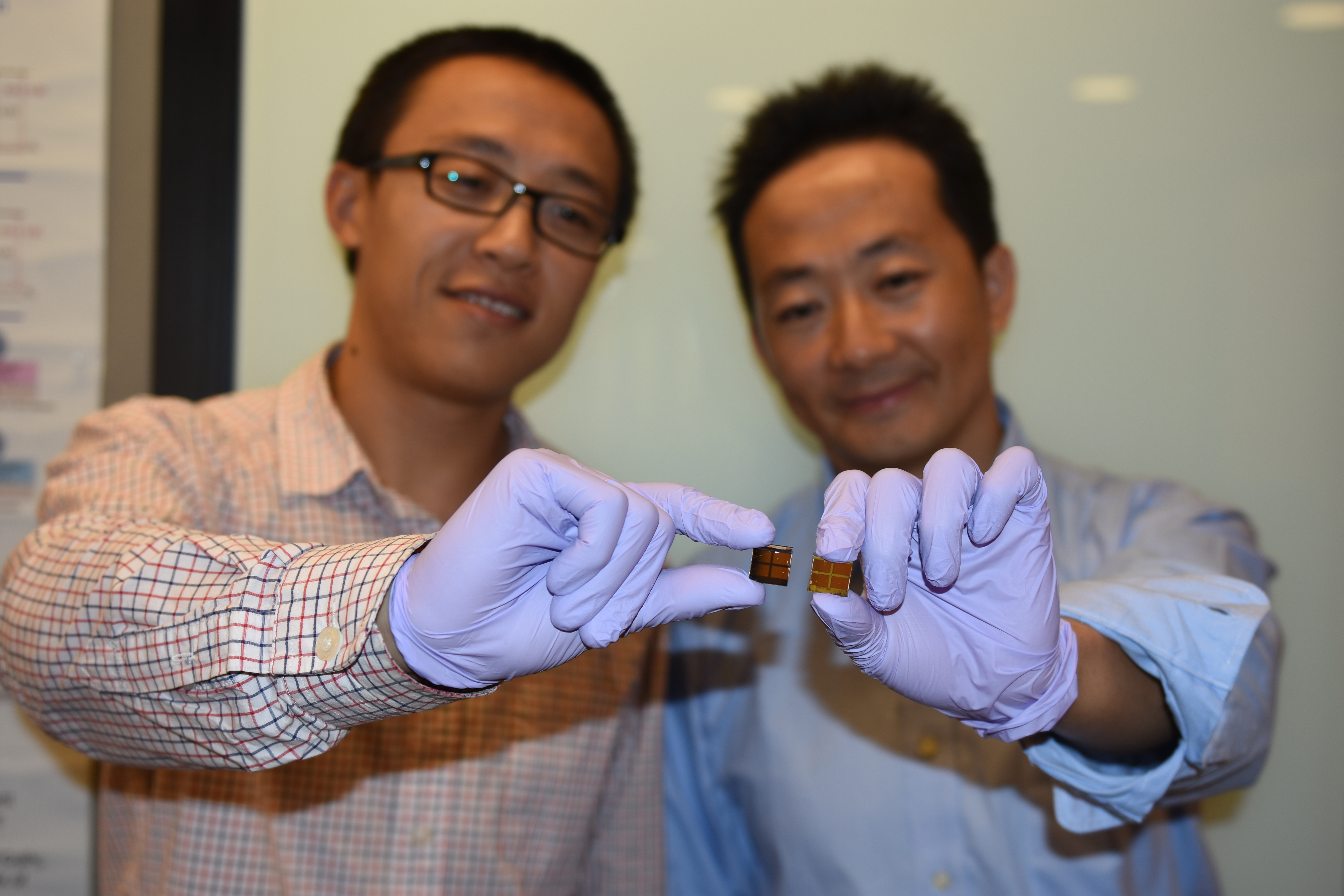 作製されたばかりのペロブスカイト太陽電池を手に持つジャン・イェン博士（左）。シェンハオ・ワン博士（右）が持っている試作品からも分かるように、劣化したMAPbI3ペロブスカイト太陽電池はかなり変色している。