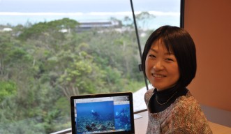 Masako Nakamura in front of a pc screen in a room with a big glass window over the mountain and ocean
