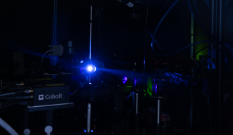 A photograph of a blue laser light hitting a reflective surface inside a complicated spectroscopy setup, housed in a dark area.