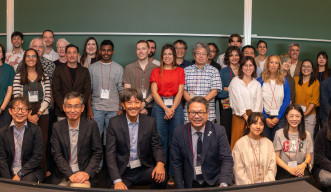 A large group of workshop participants gathered in a seminar room, standing and crouched in rows.