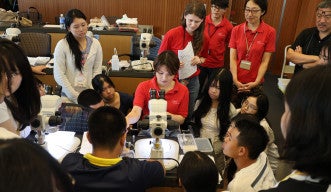 Students observe MTS members preparing ant specimens under a microscope