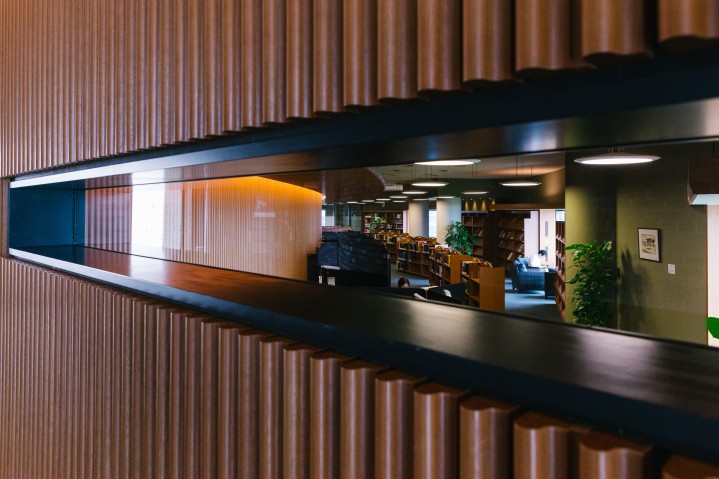 View through narrow window of person in white shirt sitting near window in library.
