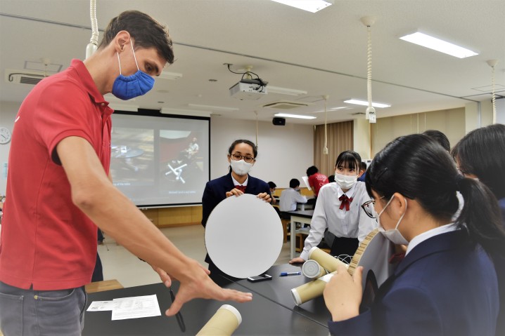 Students gathering around a table listening to an adult speaker