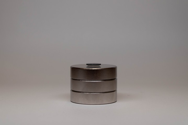 A profile view of a black graphite disk floating above a stack of three, shiny magnets. One can clearly see the separation between magnets and the disk.