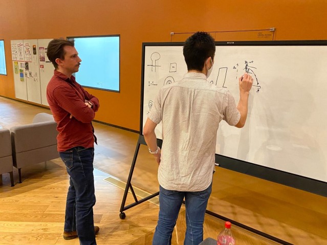 A person writing on a whiteboard while another person watches