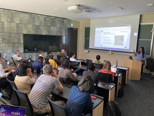 A speaker presenting in front of a screen to an audience seated in a lecture room