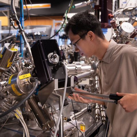 A researcher operating complicated machinery composed of shiny metal tubes and cylinders.