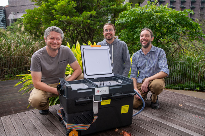 A photo of Peter Babiak, John Parker, and Zdenek Lajbner behind the newly developed cephalopod egg incubator, a large black box with wheels. 