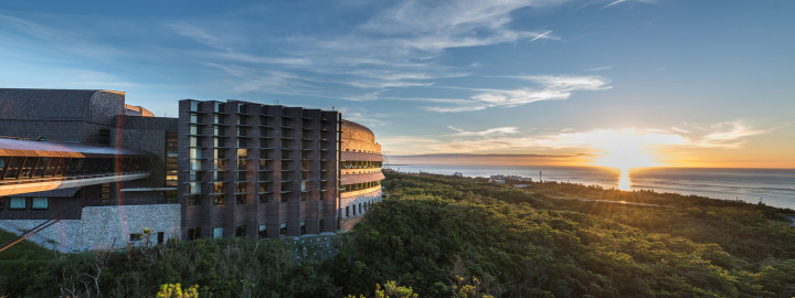 An oval‑shaped building in the green landscape with the sunset in the background