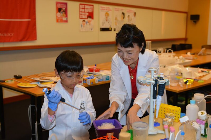 A woman and a child wearing white lab coats conducting an experiment in a laboratory