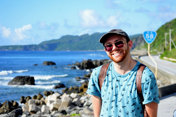 Photo of a smiling man standing by the deep blue sea.