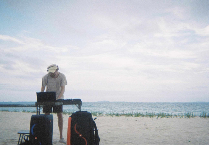 Photograph of a man behind a DJ-set on a beach.