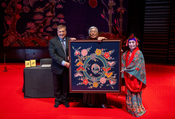 At the signing ceremony held prior to the performance, Toshikazu Tamaki (center), President of the Traditional Music Association of the Nomura School of Ryukyuan Classical Music, and dancer and bingata artist Kazuko Zukeyama (right) presented a bingata artwork to Jonathan Ray, OIST Vice President for Communication and Public Relations. Ms. Zukeyama also created the stage backdrop for the performance. 