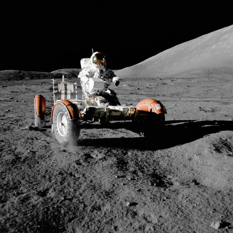 Color photograph of an astronaut driving a lunar rover on the Moon's surface. 