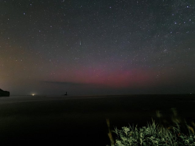A long exposure photo reveals the faint, red glow of an aurora just above the horizon. The sky above is dark and filled with stars.
