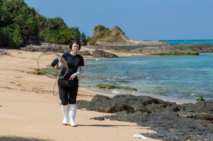 A lady standing on the beach holding a circle equipment.