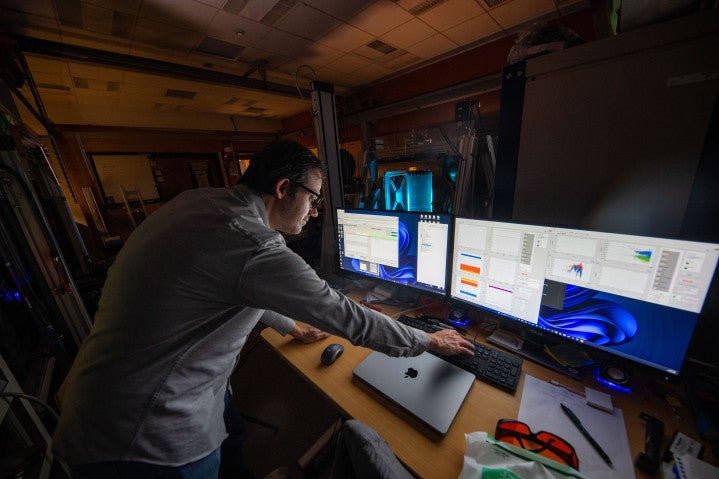 A researcher in a white coat looking at computer screens