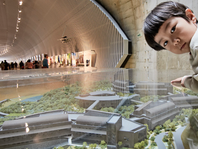 A child pausing beside the scale model of OIST campus buildings