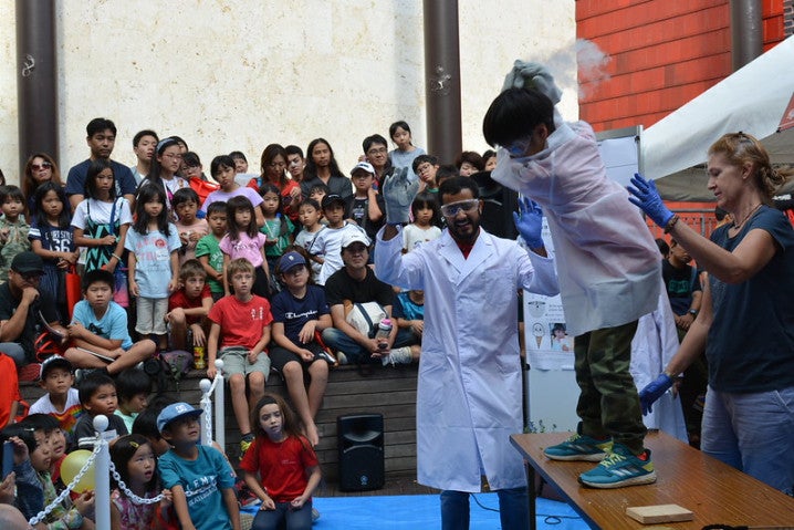 A child performing with scientists surrounded by audience