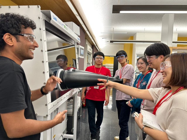 smiling people gathering around a lab equipment