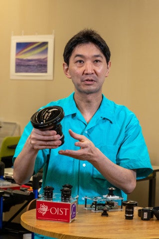 Ryuho Kataoka explains his auroral imagers, holding up a large aperture used to get high resolution images. On the table in front are the smaller versions he's developing, including prototypes for his new Mars project.