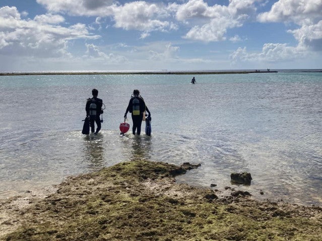 Two researchers in scuba gear wade through shin-deep water on their way to start the dive.