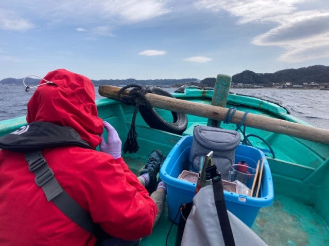A person in a red raincoat and purple lab gloves sits in a boat.