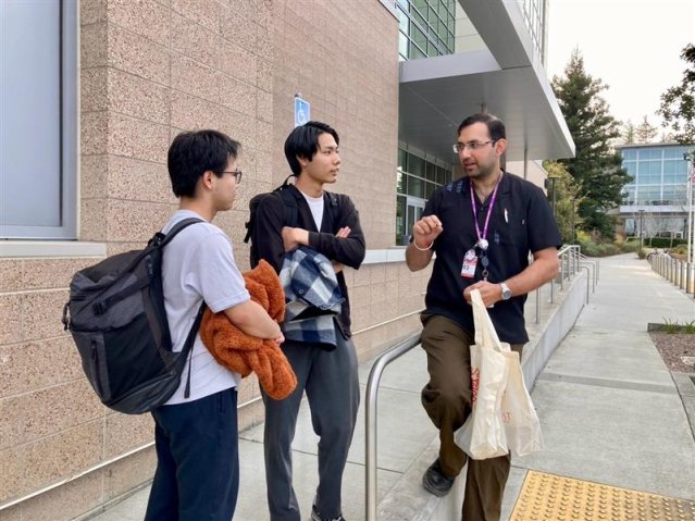 SLAC国立加速器研究所の建物の外で、研究者の話を熱心に聞き入る高校生2人。