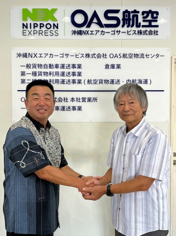 Two men shaking hands in front of OAS's name plate