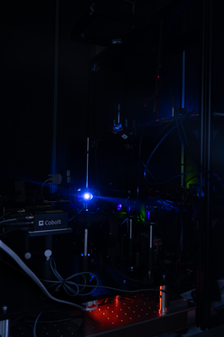 A photograph of a blue laser light hitting a reflective surface inside a complicated spectroscopy setup, housed in a dark area. 
