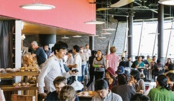 Cafe Tancha, with many people sitting, eating and talking. Pastries are sold on the left with large windows on the right