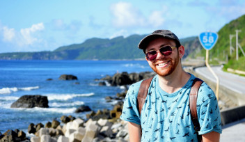 Photo of a smiling man standing by the deep blue sea.