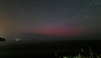 A long exposure photo reveals the faint, red glow of an aurora just above the horizon. The sky above is dark and filled with stars.