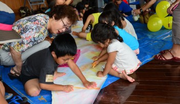 Visitors from Onna Village decorate segments of a mural depicting a life-size humpback whale.