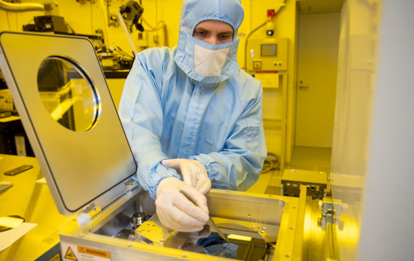 A researcher in personal protective equipment opening the hatch of a laboratory machine