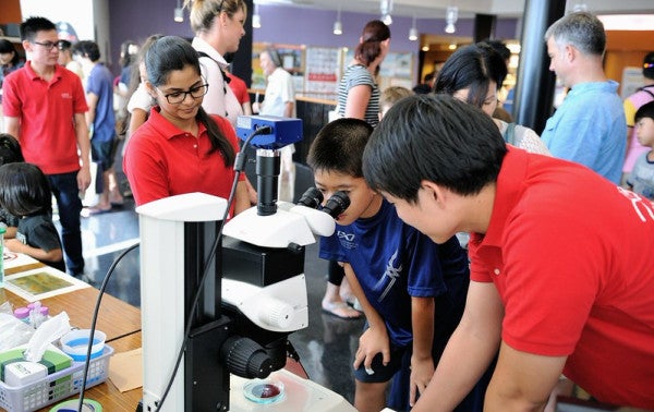 A child looking into a microscope with two staff members nearby