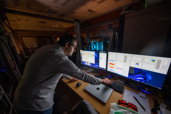 A researcher in a white coat looking at computer screens