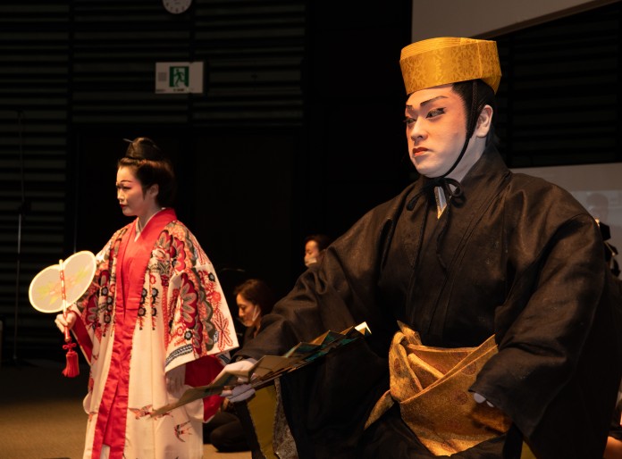 Female and male dancers dressed in traditional Ryukyuan costume dance with fans.