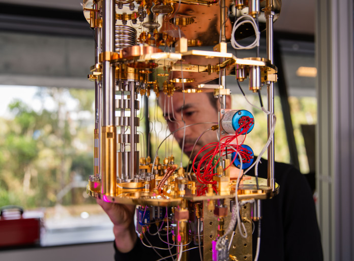 A beautiful gold machine with lots of wires in the foreground, at which a man in the background stares intently. 