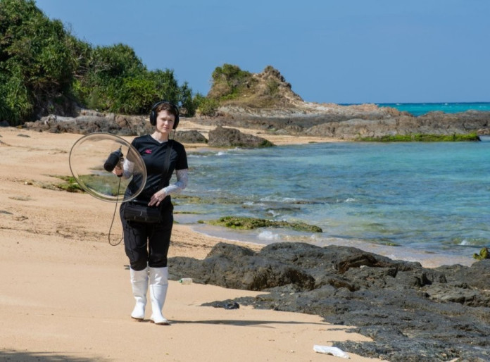 A lady standing on the beach holding a circle equipment.