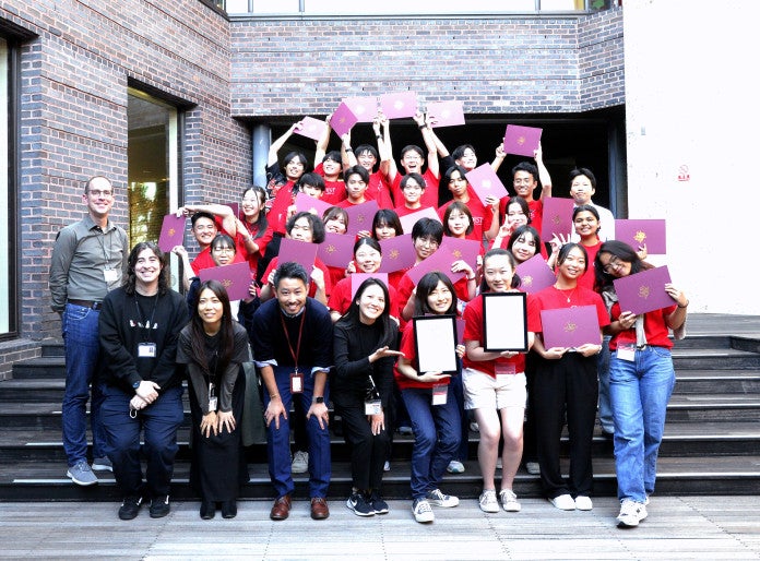 a group of students in red shirts holding certificate and people in black sirts 
