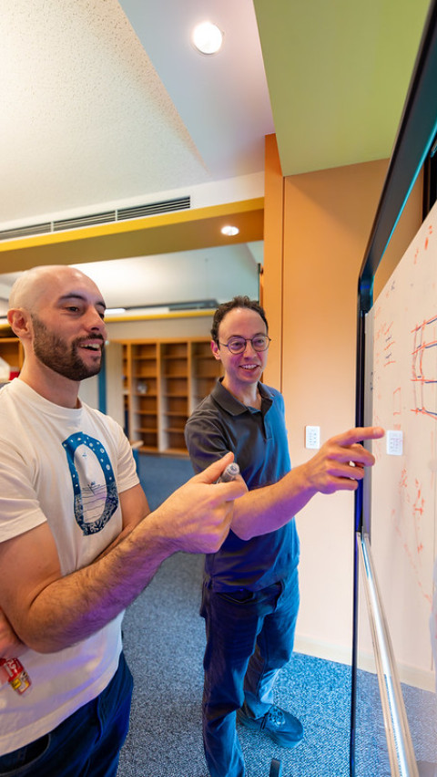 Two person talking in front of a white board.